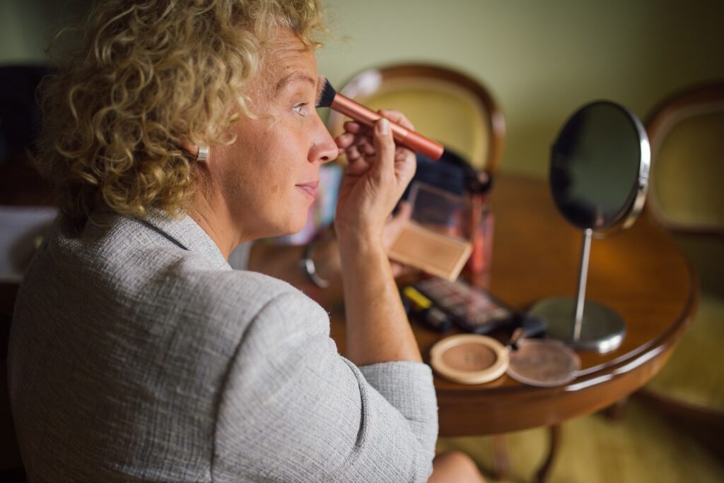Person trägt vor einem Spiegel Make-up auf und prüft den Übergang an der Kieferlinie