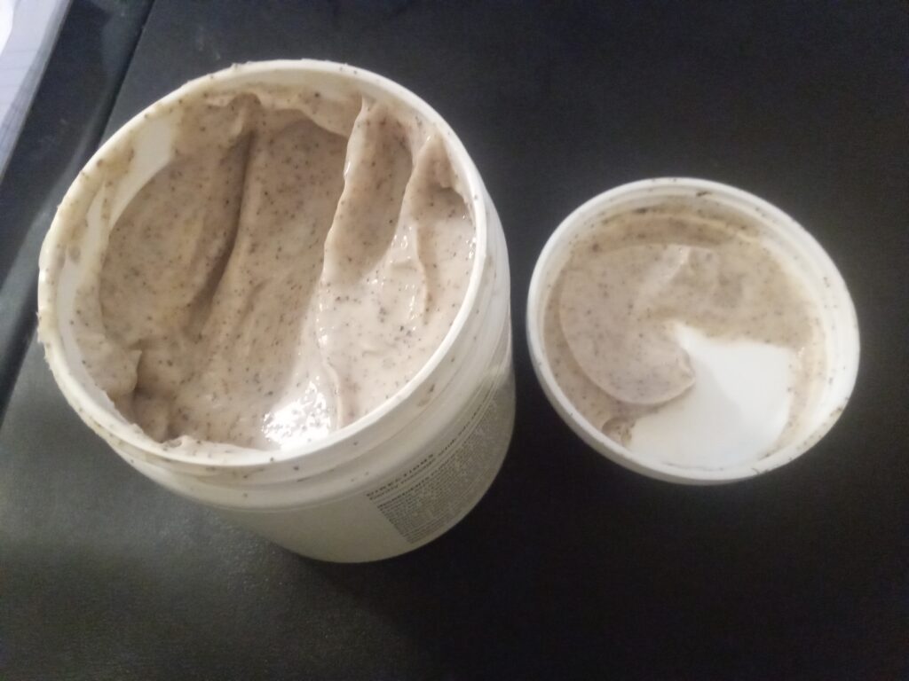 Ge&ouml;ffneter Tiegel mit k&ouml;rniger Peelingmasse neben einem feuchten Waschlappen