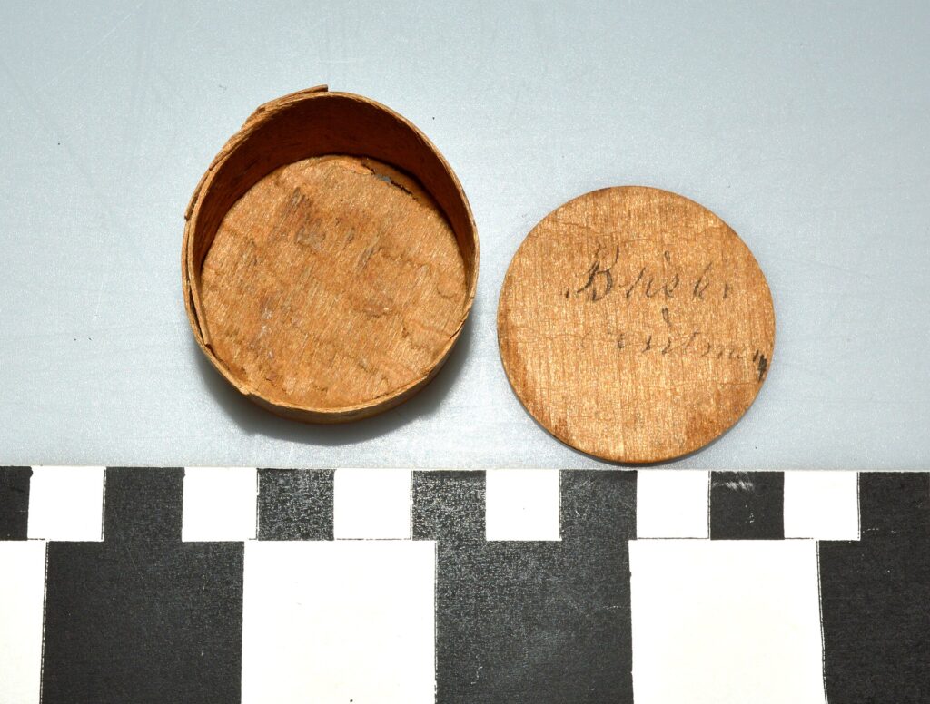 Geöffnete flache Dose mit fetthaltiger Salbe steht neben ihrem Deckel auf einem Tisch
