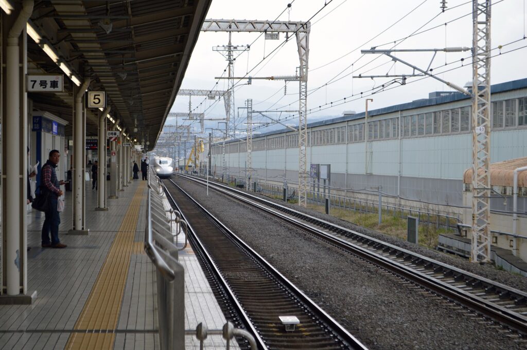 Menschen mit Winterm&auml;nteln warten an einem offenen Bahnsteig bei grauem Wetter