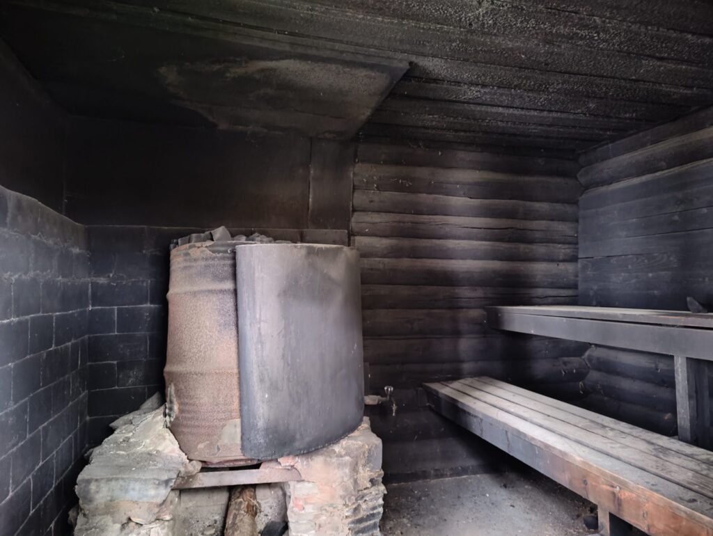 Holzkelle und Eimer stehen neben gl&uuml;hend hei&szlig;en Steinen auf einem Saunaofen