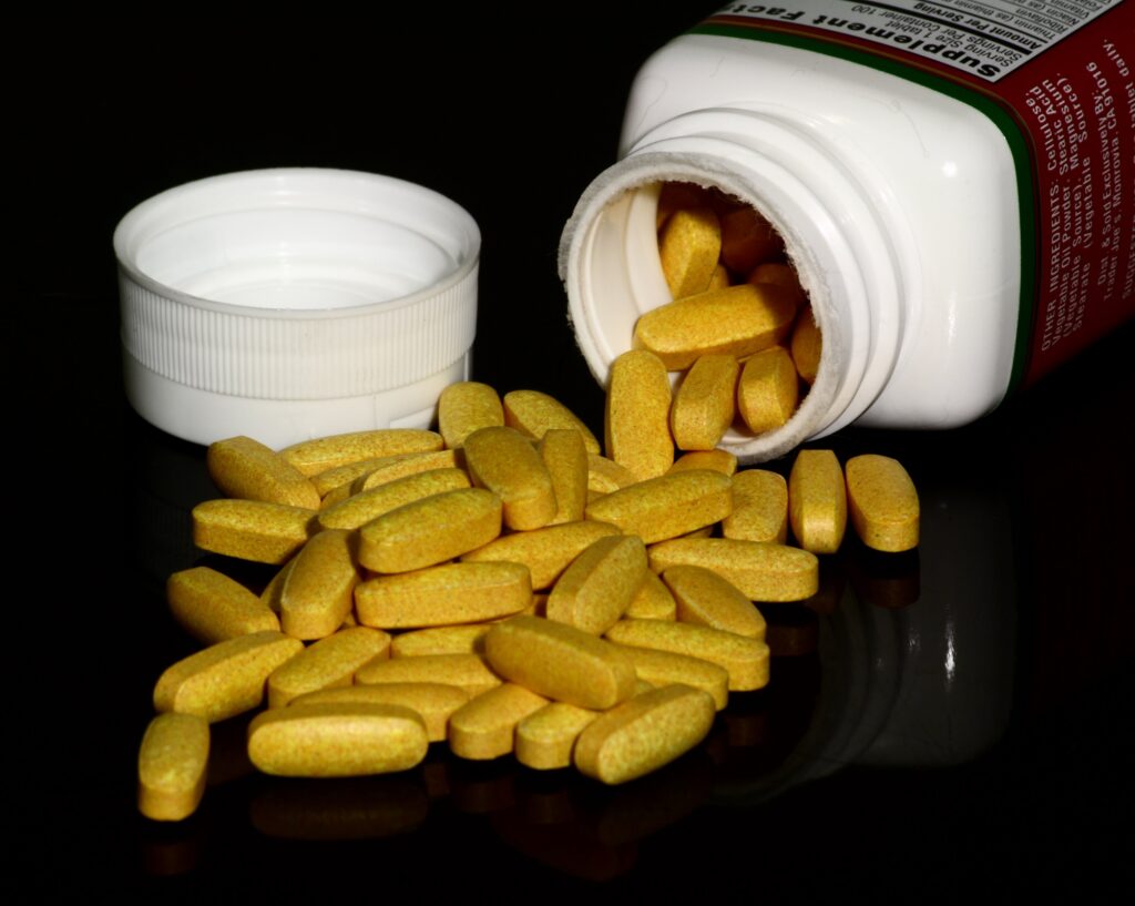 Ge&ouml;ffnete Dose mit Tabletten und einige Kapseln daneben auf einer wei&szlig;en Fl&auml;che