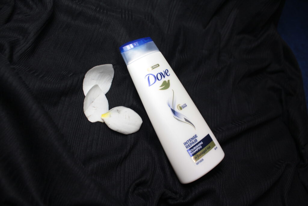 Shampooflasche steht am Rand einer Duschwanne, im Hintergrund gefliestes Bad
